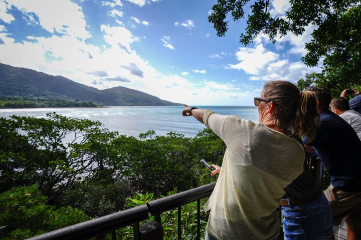 Woman pointing at coastal view with mountains and trees under a cloudy sky.